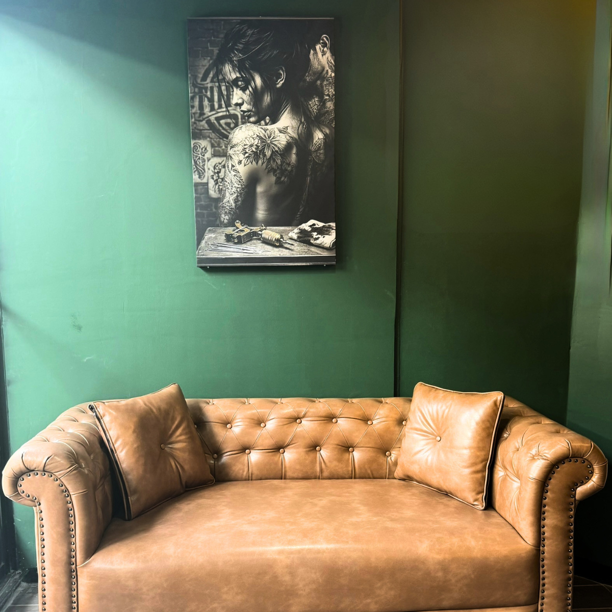 Studio waiting lounge with a Chesterfield sofa beneath a framed black and grey tattoo portrait