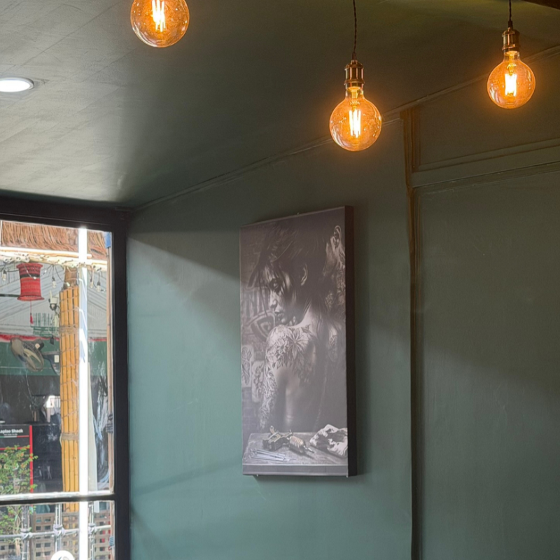 Studio interior with Edison pendant lights and framed tattoo artwork on a green wall