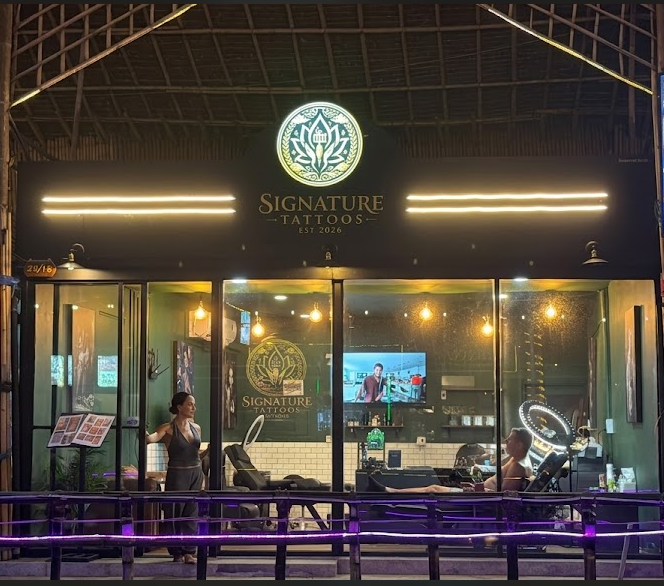 Signature Tattoos studio storefront at night with illuminated gold logo sign and clients inside